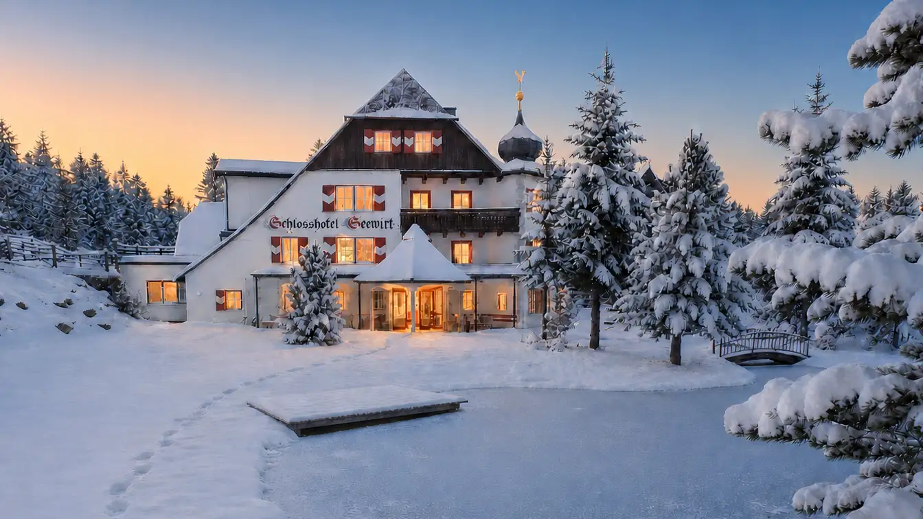 Das Schlosshotel Seewirt in der Abenddämmerung, mit warm erleuchteten Fenstern, verschneiten Zirben und dem zugefrorenen Teich